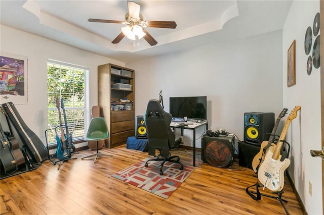 home office with ceiling fan, a raised ceiling, and light hardwood / wood-style flooring