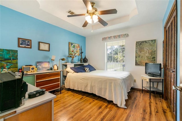 bedroom featuring a closet, a raised ceiling, light wood-type flooring, and ceiling fan