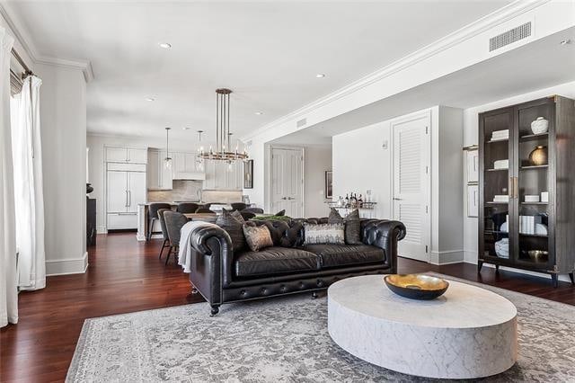 living room featuring crown molding, an inviting chandelier, and dark wood-type flooring