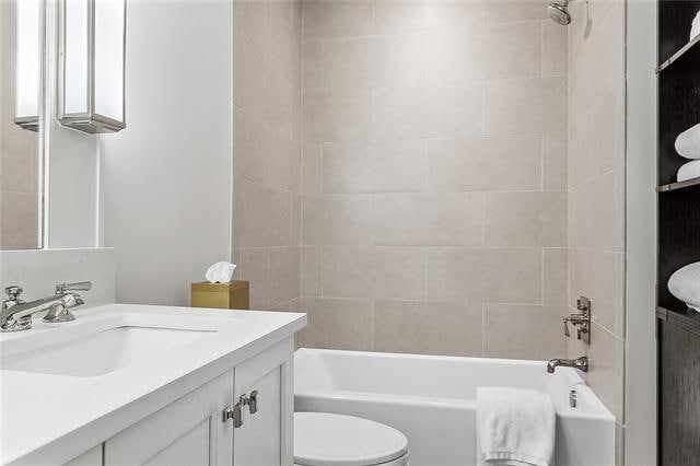 full bathroom featuring tiled shower / bath, vanity, and toilet