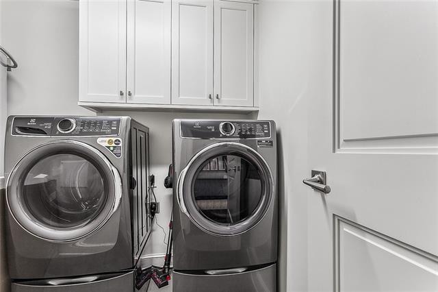 clothes washing area with washer and dryer and cabinets