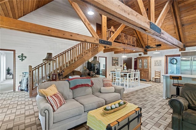 living room with ceiling fan with notable chandelier, beam ceiling, high vaulted ceiling, wooden walls, and wooden ceiling