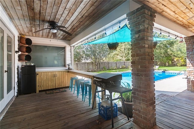 deck featuring ceiling fan, a fenced in pool, and an outdoor bar