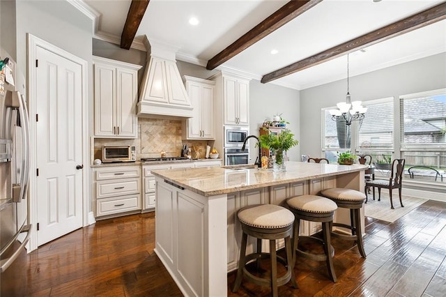 kitchen featuring dark wood-type flooring, a center island with sink, hanging light fixtures, light stone counters, and stainless steel appliances