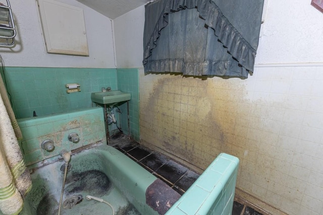 bathroom with a bath, sink, and tile walls