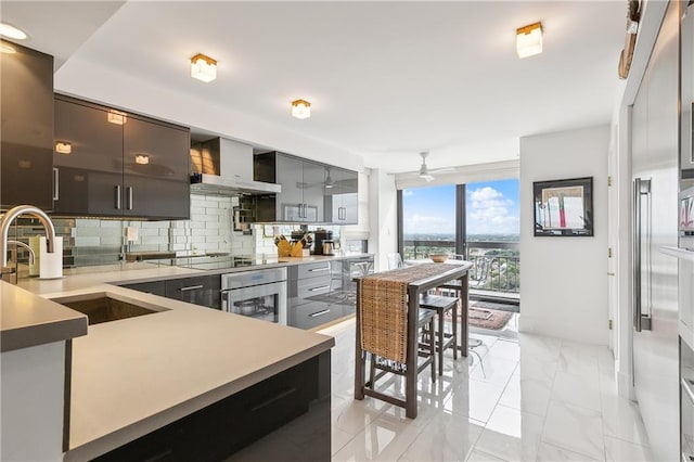 kitchen with sink, wall chimney range hood, decorative backsplash, stainless steel appliances, and ceiling fan