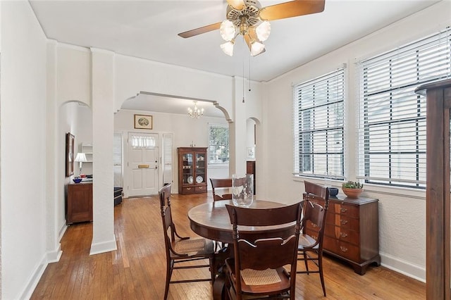 dining space with light hardwood / wood-style flooring, ceiling fan with notable chandelier, and decorative columns