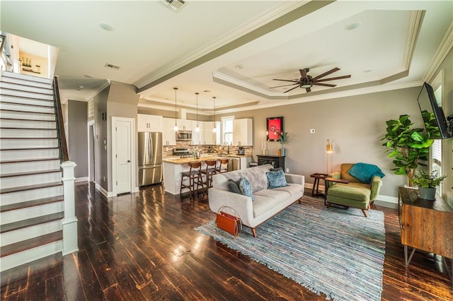 living room with ceiling fan, a raised ceiling, dark hardwood / wood-style floors, and crown molding