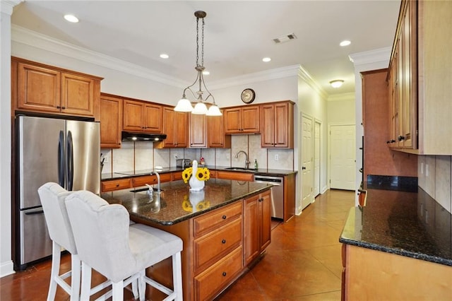 kitchen featuring a kitchen island with sink, pendant lighting, sink, stainless steel appliances, and ornamental molding