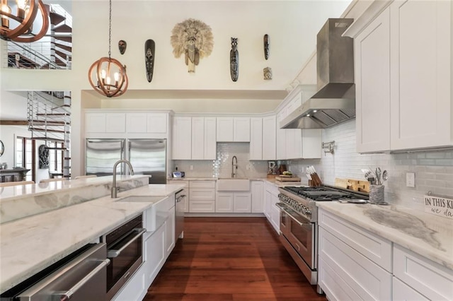 kitchen with pendant lighting, white cabinets, wall chimney range hood, and high quality appliances