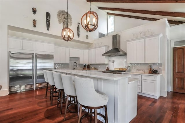 kitchen with wall chimney exhaust hood, high end refrigerator, pendant lighting, and white cabinets