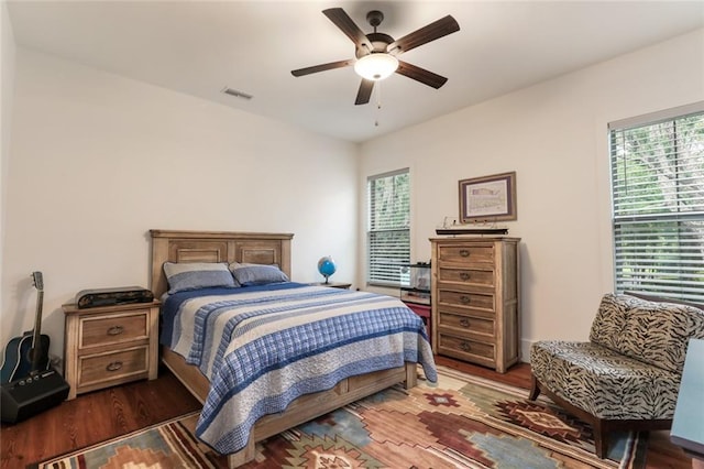 bedroom with dark wood-style floors, ceiling fan, multiple windows, and visible vents