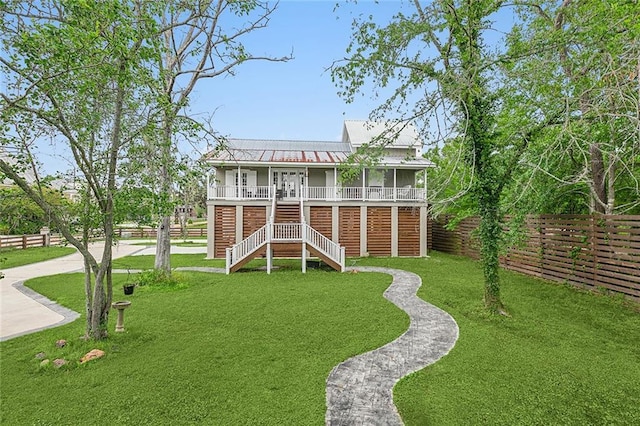 view of front facade with metal roof, fence private yard, stairs, french doors, and a front lawn