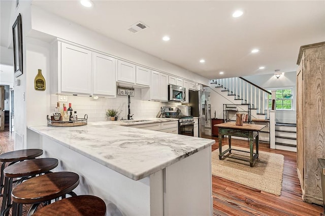 115 Holly St, Mandeville, LA 70448 - kitchen featuring stainless steel appliances, a sink, wood finished floors, a kitchen bar, and recessed lighting