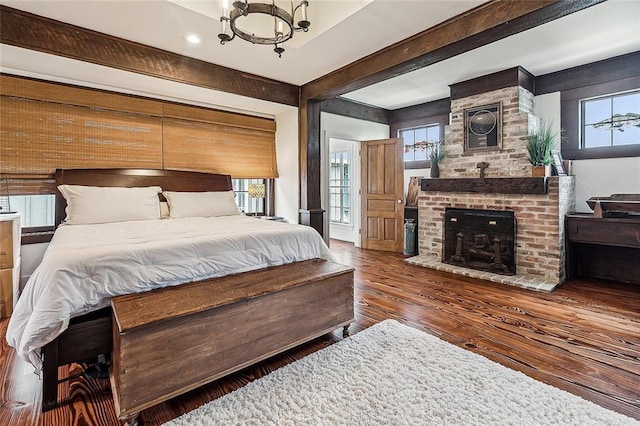 bedroom with a brick fireplace, an inviting chandelier, dark wood-style flooring, and beamed ceiling