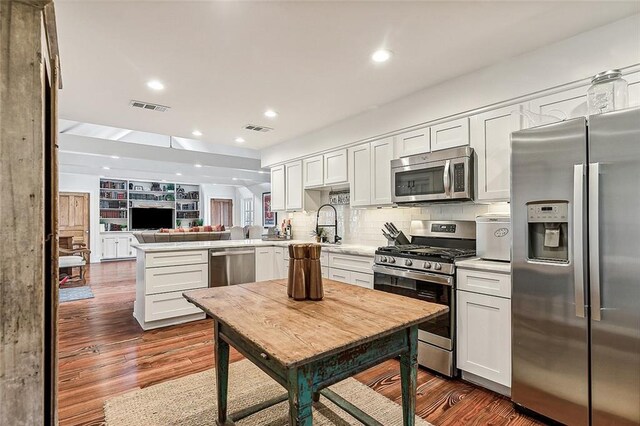 115 Holly St, Mandeville, LA 70448 - kitchen featuring appliances with stainless steel finishes, a peninsula, open floor plan, decorative backsplash, and light countertops