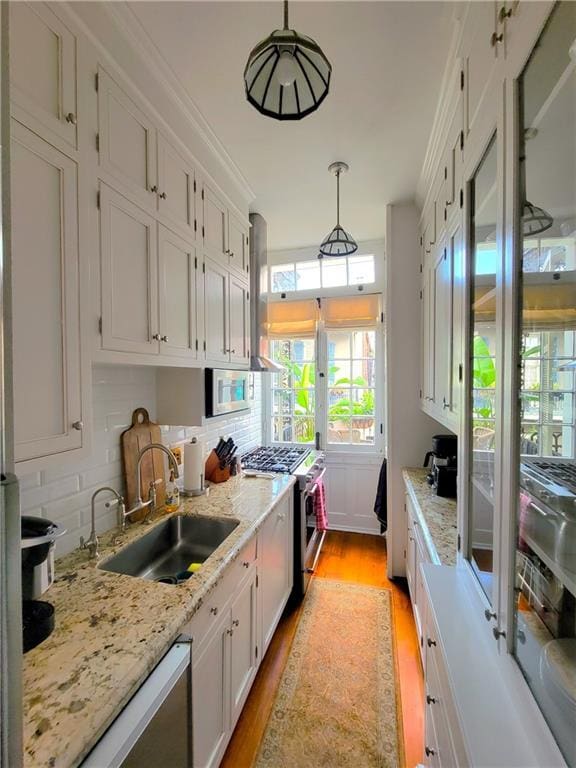 kitchen with sink, stainless steel appliances, hanging light fixtures, white cabinets, and light wood-type flooring