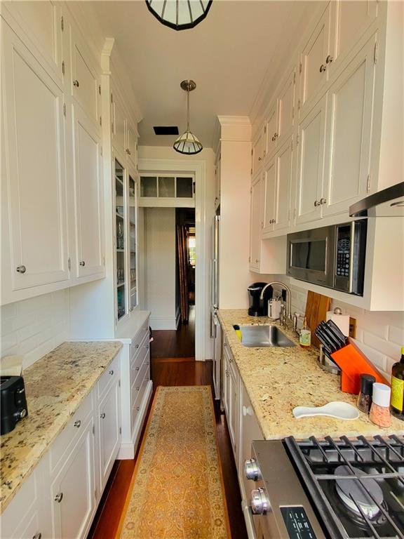 kitchen with light stone countertops, sink, white cabinets, dark hardwood / wood-style floors, and hanging light fixtures