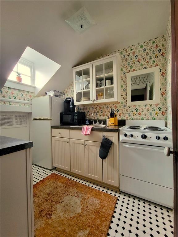 kitchen with lofted ceiling, white appliances, sink, and cream cabinets