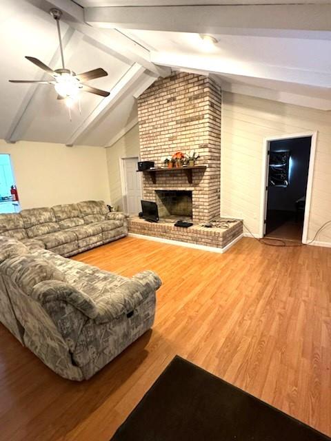 living room featuring vaulted ceiling with beams, ceiling fan, hardwood / wood-style flooring, and a fireplace