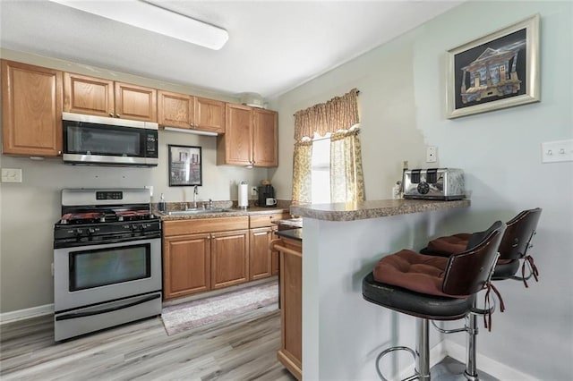 kitchen featuring sink, light hardwood / wood-style flooring, appliances with stainless steel finishes, kitchen peninsula, and a breakfast bar area