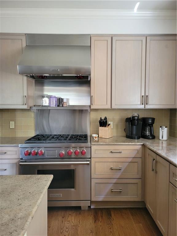 kitchen with light stone countertops, dark hardwood / wood-style flooring, backsplash, designer range, and wall chimney range hood