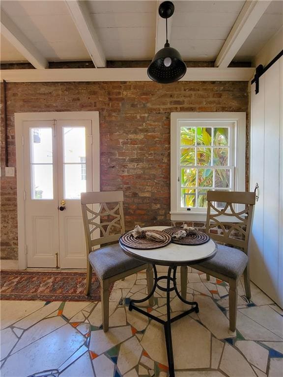 dining space featuring a barn door, a wealth of natural light, beamed ceiling, and brick wall