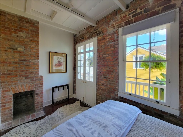 bedroom with dark hardwood / wood-style floors, beam ceiling, brick wall, and a brick fireplace