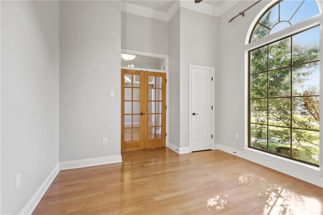 empty room featuring light hardwood / wood-style flooring, ornamental molding, a towering ceiling, and french doors