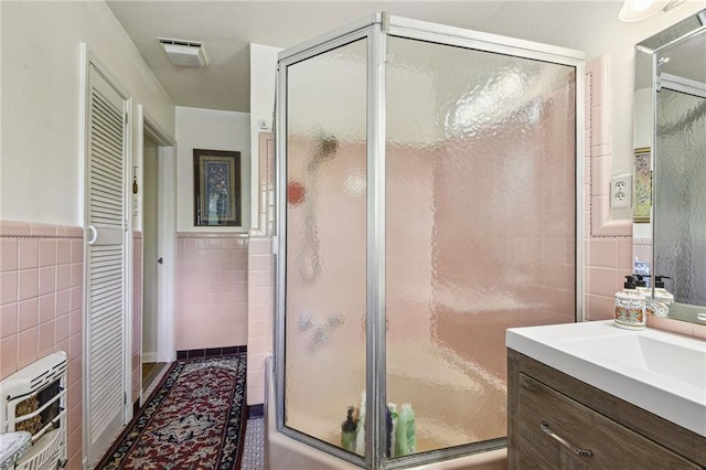 bathroom with a shower with door, tile walls, tile patterned flooring, heating unit, and vanity