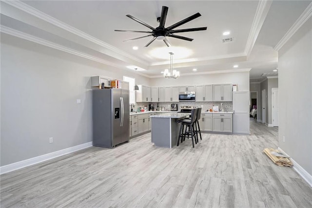 kitchen with gray cabinets, a center island, a kitchen bar, stainless steel appliances, and decorative light fixtures