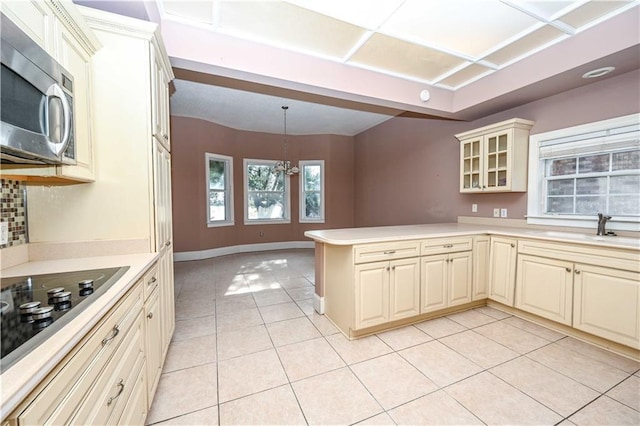 kitchen with cream cabinetry, kitchen peninsula, light tile patterned floors, decorative light fixtures, and sink