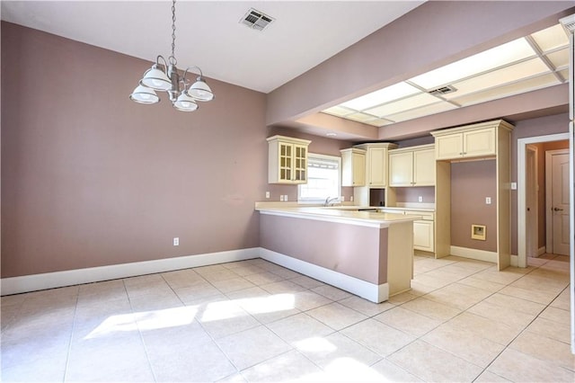 kitchen featuring light tile patterned flooring, hanging light fixtures, kitchen peninsula, cream cabinetry, and a notable chandelier