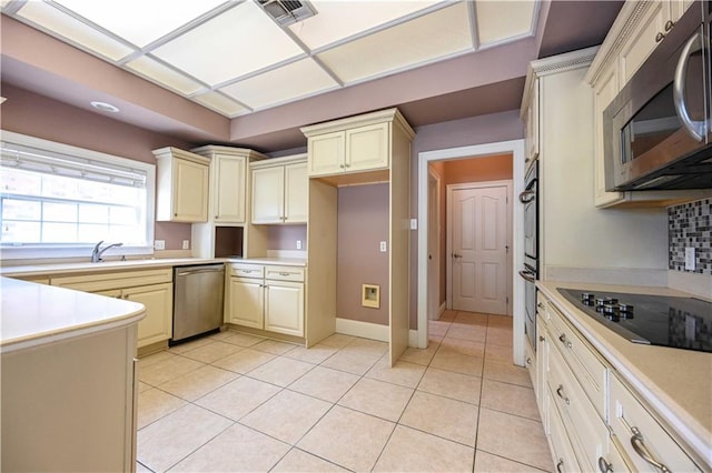 kitchen featuring stainless steel appliances, cream cabinetry, light tile patterned floors, and decorative backsplash