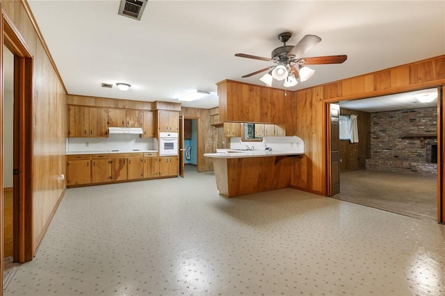 kitchen with brick wall, kitchen peninsula, wood walls, white oven, and ceiling fan