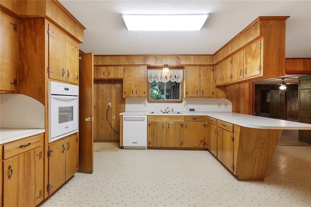 kitchen with ceiling fan, kitchen peninsula, sink, and white appliances