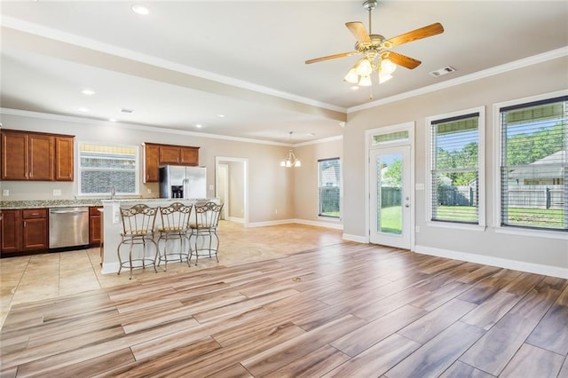 kitchen featuring light hardwood / wood-style flooring, ornamental molding, a kitchen bar, appliances with stainless steel finishes, and ceiling fan with notable chandelier