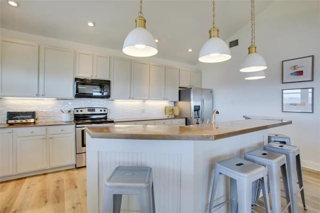 kitchen with a kitchen island with sink, a breakfast bar area, white cabinets, appliances with stainless steel finishes, and decorative light fixtures