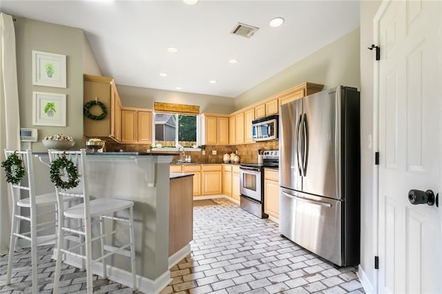 kitchen featuring decorative backsplash, kitchen peninsula, a breakfast bar area, stainless steel appliances, and light brown cabinetry