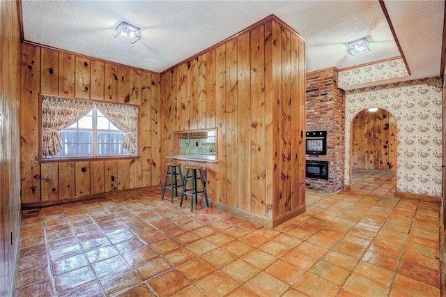 kitchen featuring a textured ceiling, light tile patterned flooring, wood walls, and a breakfast bar area