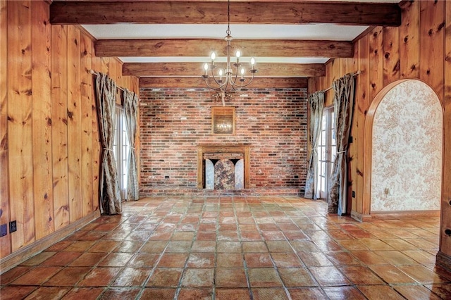 unfurnished living room featuring beam ceiling, wood walls, brick wall, and an inviting chandelier