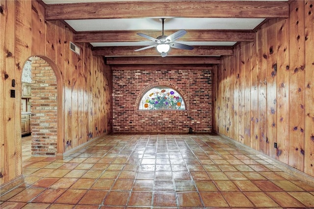 spare room featuring ceiling fan, brick wall, wooden walls, and beam ceiling