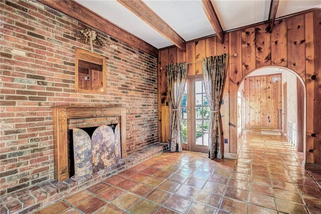 unfurnished living room with beam ceiling, wood walls, french doors, and brick wall