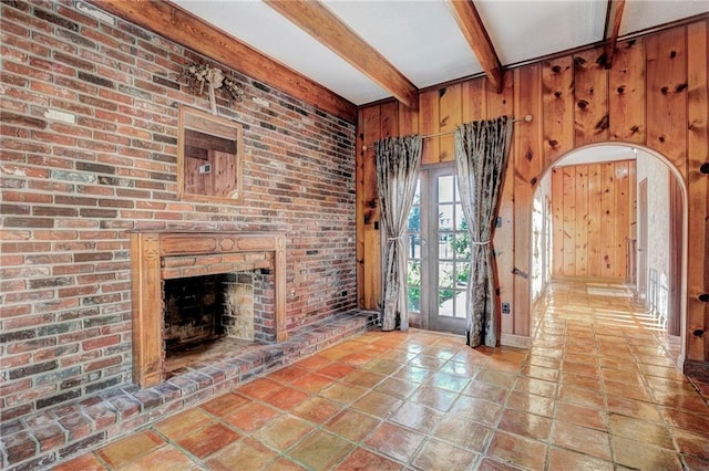 unfurnished living room with beam ceiling, wood walls, brick wall, and a brick fireplace