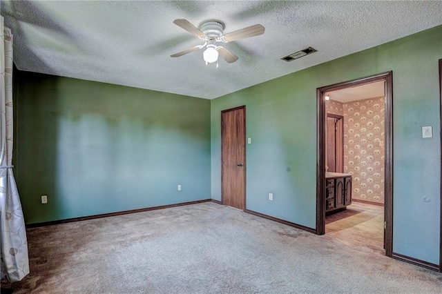 unfurnished bedroom featuring a textured ceiling, ensuite bath, ceiling fan, and light colored carpet