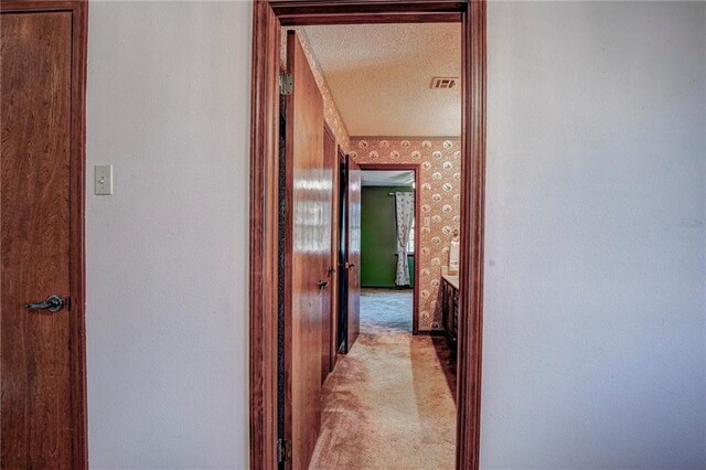 hall featuring a textured ceiling and light carpet