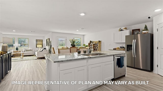 kitchen with appliances with stainless steel finishes, an island with sink, white cabinets, light stone countertops, and light wood-type flooring