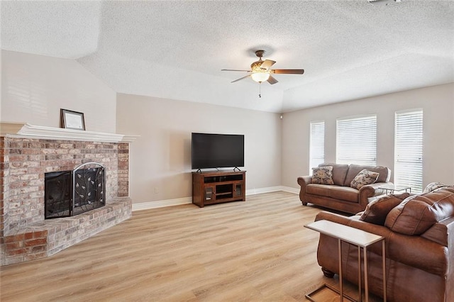 living room with ceiling fan, light hardwood / wood-style floors, a textured ceiling, a fireplace, and vaulted ceiling