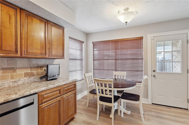 kitchen with a textured ceiling, light hardwood / wood-style floors, backsplash, light stone countertops, and stainless steel dishwasher