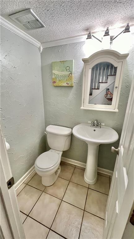 bathroom featuring ornamental molding, toilet, tile patterned flooring, and a textured ceiling